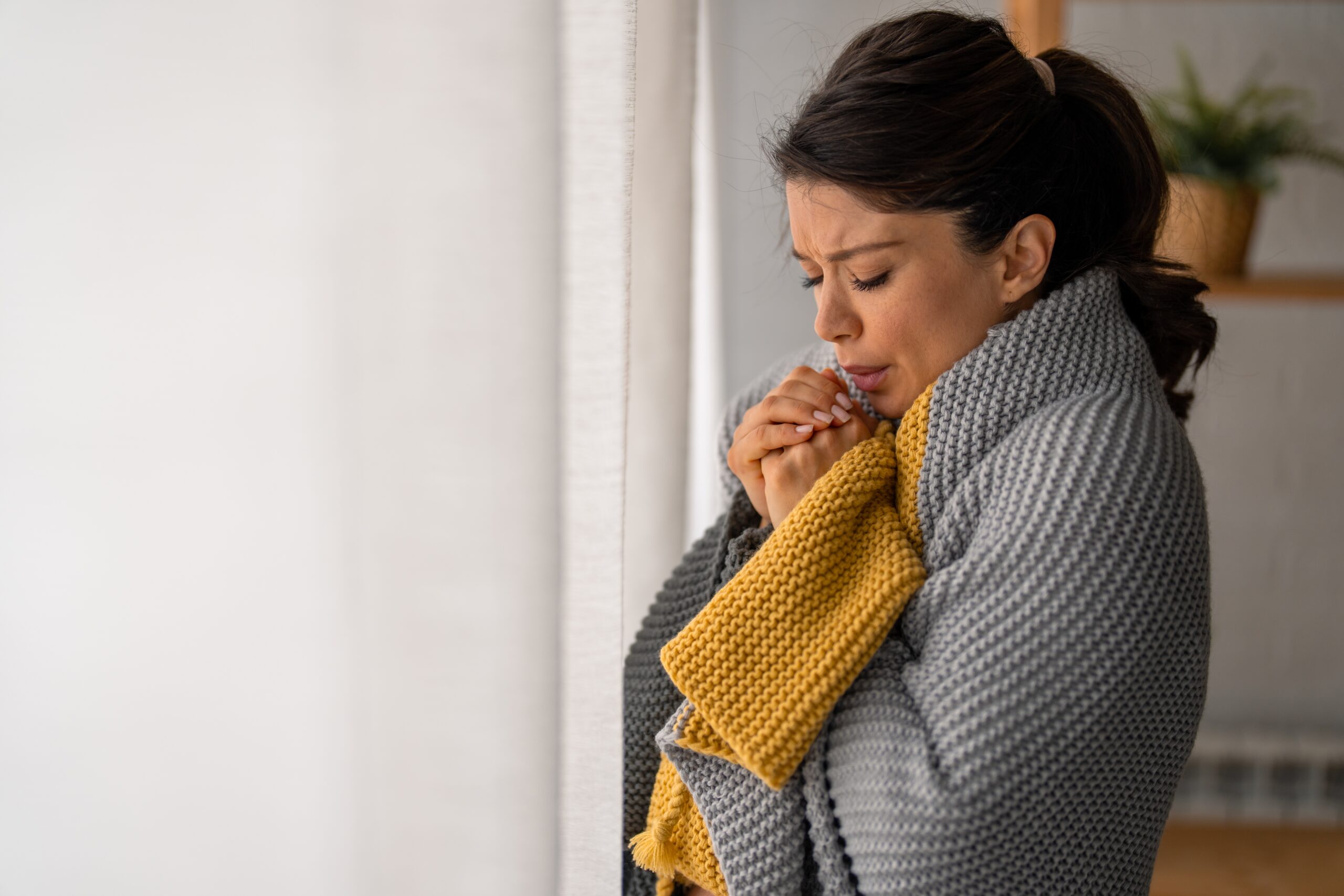 woman cold in house wearing sweater and scarf poor insulation